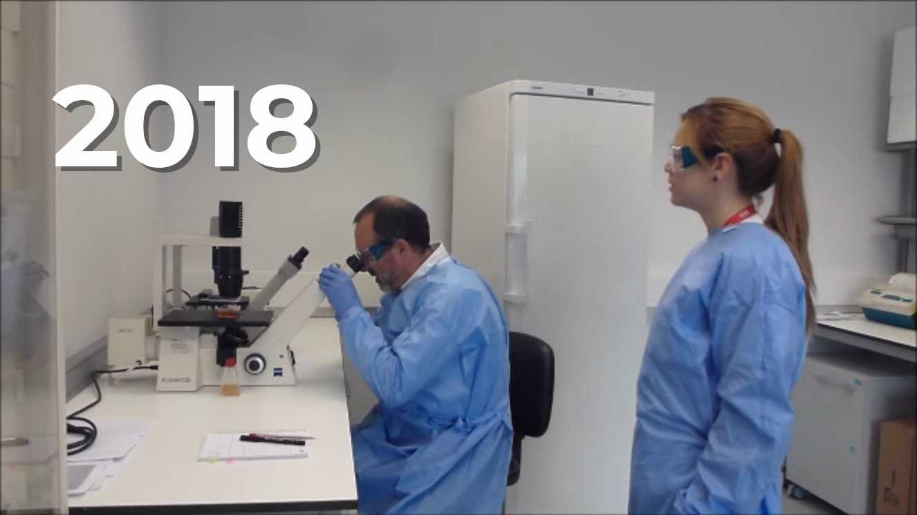 Médico al fondo mirando por un microscopio y doctora mirando lo que hace