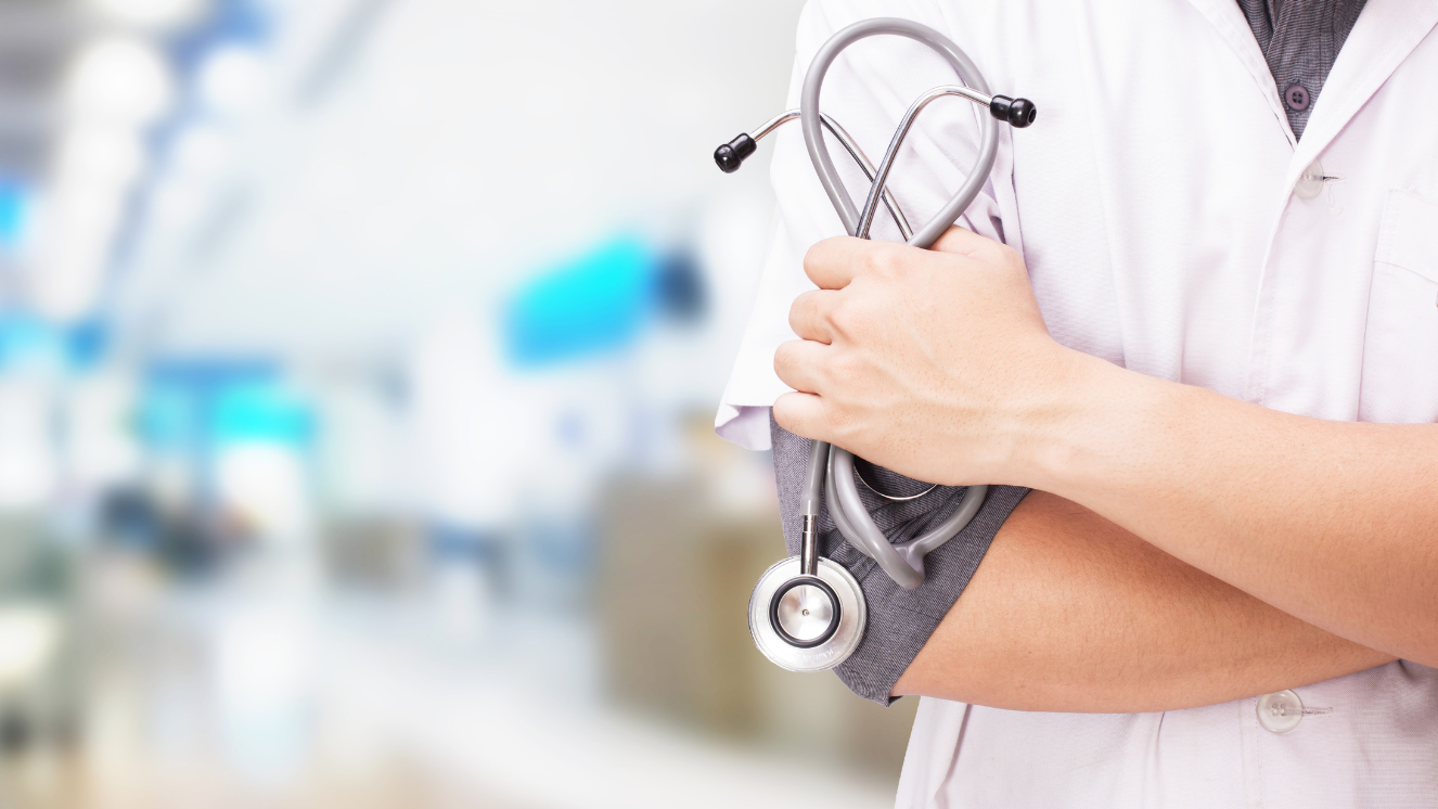 primer plano del torso de un médico joven con bata y con el fonendo en la mano y fondo desenfocado