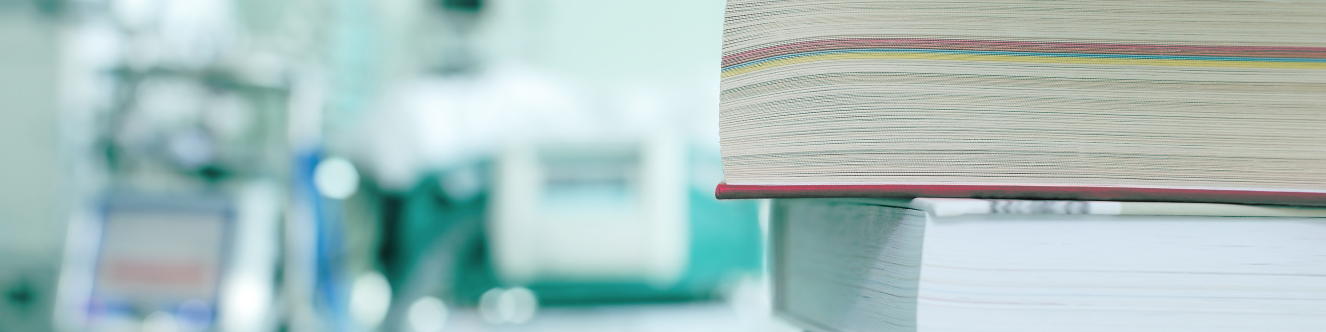 en primer plano a la derecha pila de cuatro libros y de fondo desenfocado aparatos médicos
