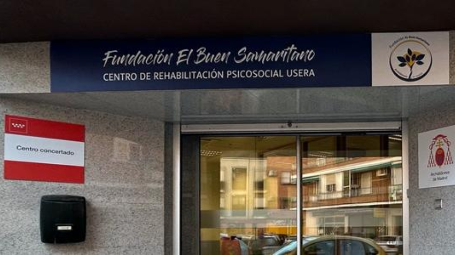 Entrada puerta doble de cristal en edificio gris y con rótulo grande azul sobre la puerta