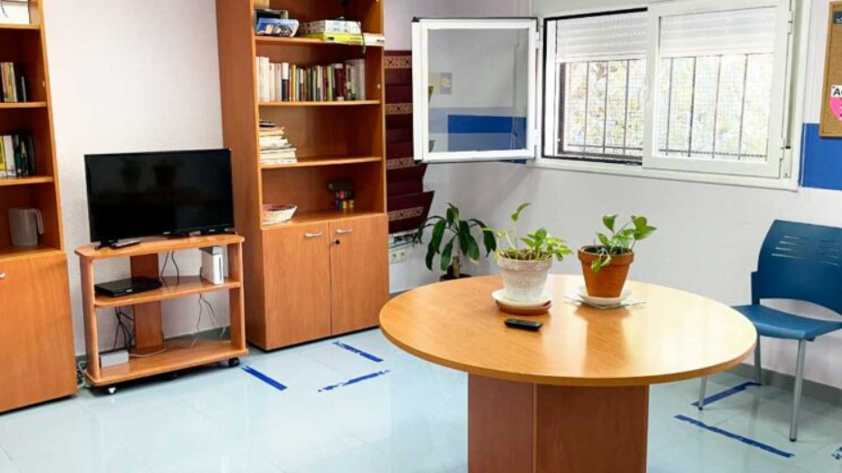 Habitación con mesa en el medio, mueble alto detrás de madera de pino y ventana a la derecha y se ve parte de un sofá