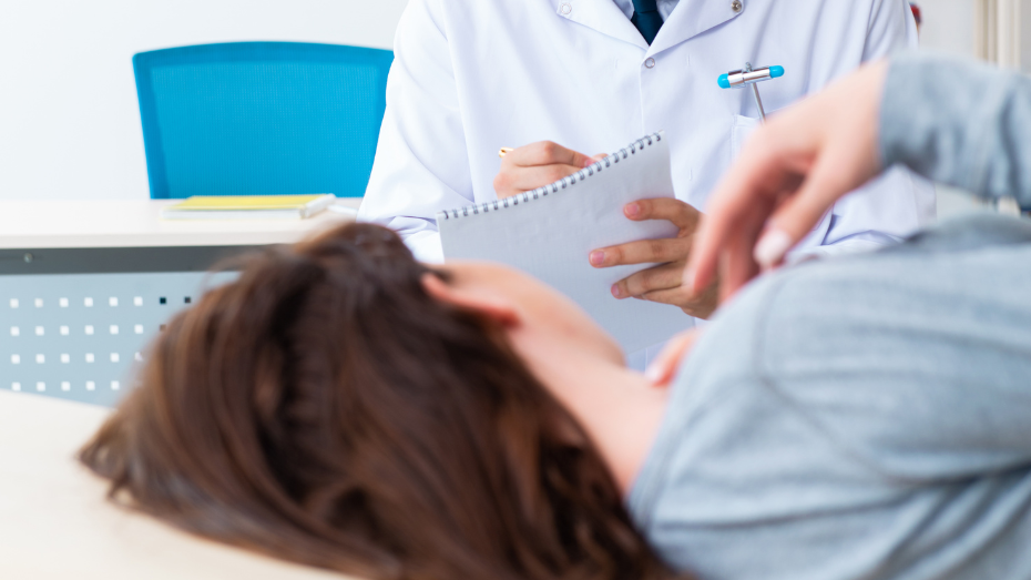 Primer plano de mujer echada en cama de espaldas y torso de frente de médico tomando notas