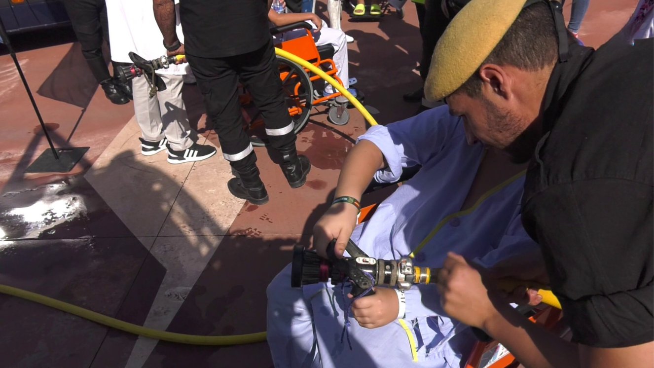 Bomberos con paciente niño enseñando a usar manguera