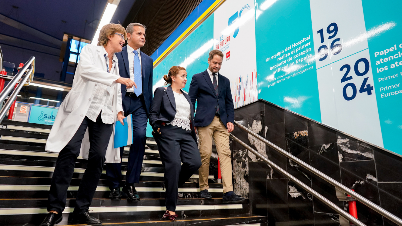 4 personas bajan las escaleras del metro mientras contemplan imágenes en la pared