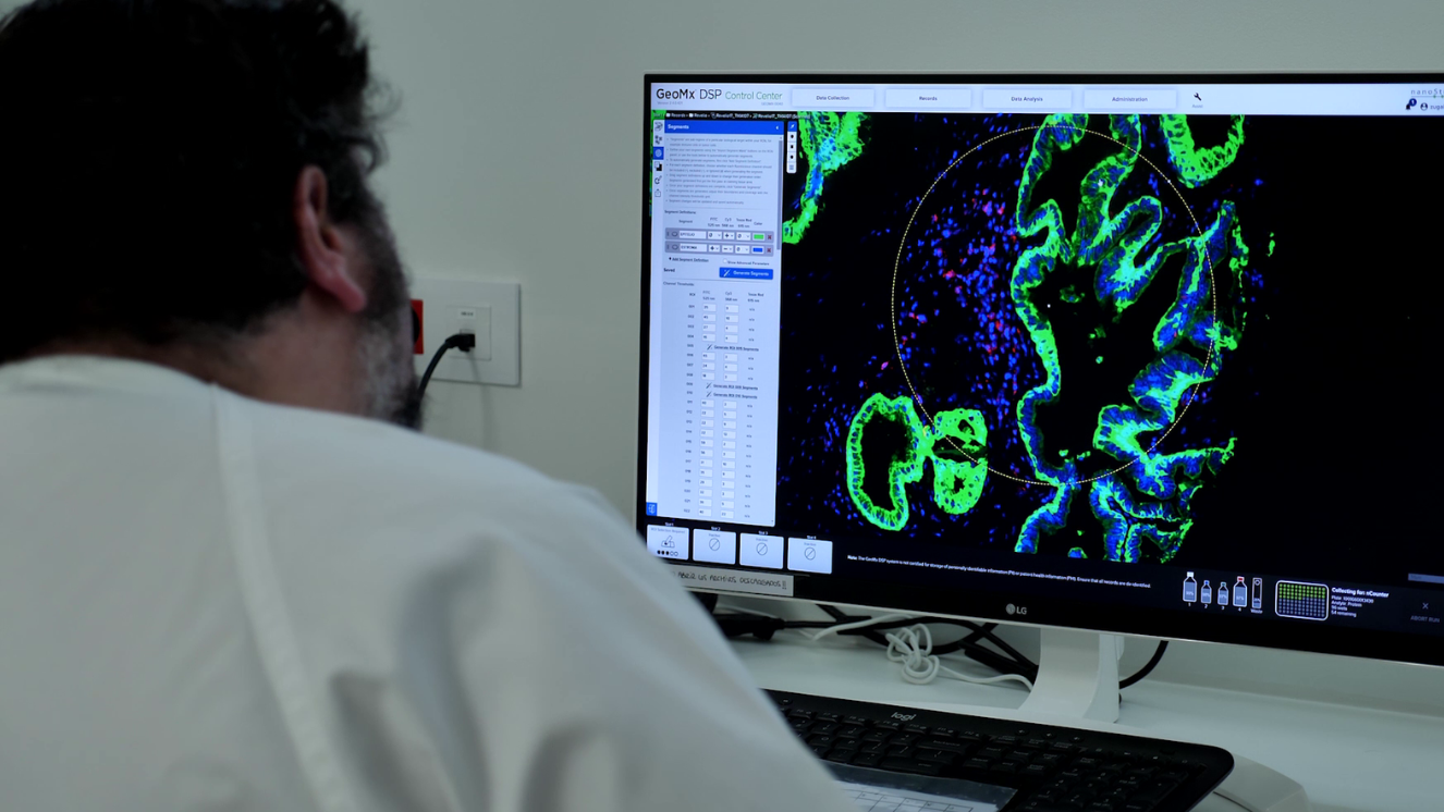 investigador con bata de espaldas frente a pantalla con luces verdes y moradas