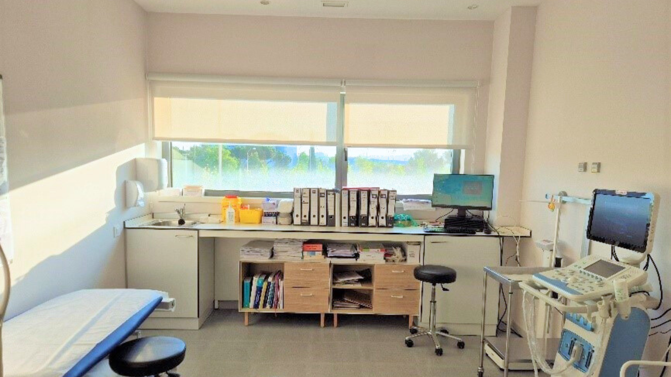 Sala con camilla a la izquierda, armario bajo de madera clara al fondo y a la derecha aparatos sanitarios