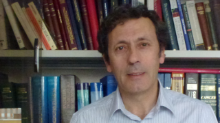 Hombre pelo moreno algo rizado, media edad, con fondo de librería