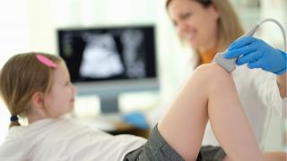 reumatología pediátrica niña tumbada y médica analizando rodilla