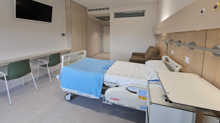 Cama en primer plano y sofá al fondo y enfrente dos sillas verdes