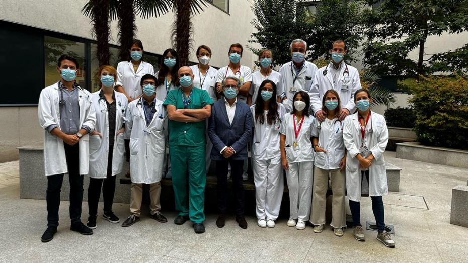 médicos y médicas con bata blanca posando con jardín de fondo