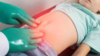 Hernia manos con guantes verdes tocan la zona abdominal de un niño
