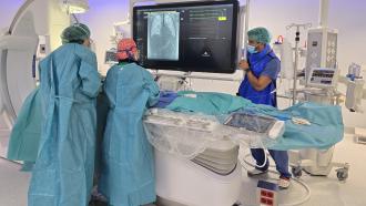 Dos cardiólogos en una sala de hemodinámica tratando a un niño tumbado y enfrente una pantalla