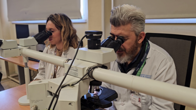 Dos investigadores con bata blanca mirando por dos microscopios