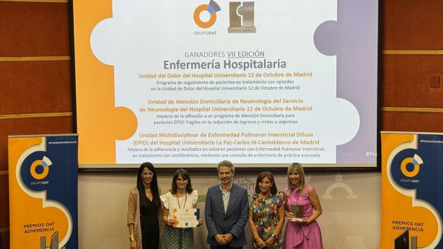 5 personas en un escenario cuatro mujeres y en el centro un hombre con diplomas y detrás una pantalla con texto