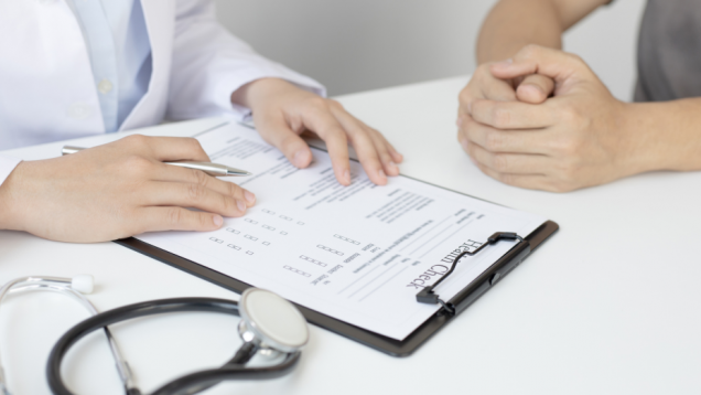 Manos de médico sobre cuestionario frente a manos de paciente sobre mesa