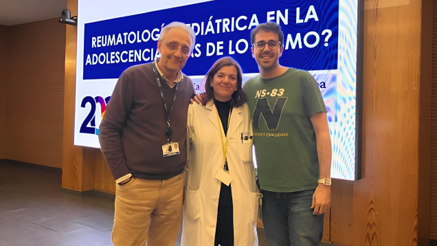 Tres personas dos hombre y en el medio una mujer posando delante de una gran pantalla con un texto con fondo azul