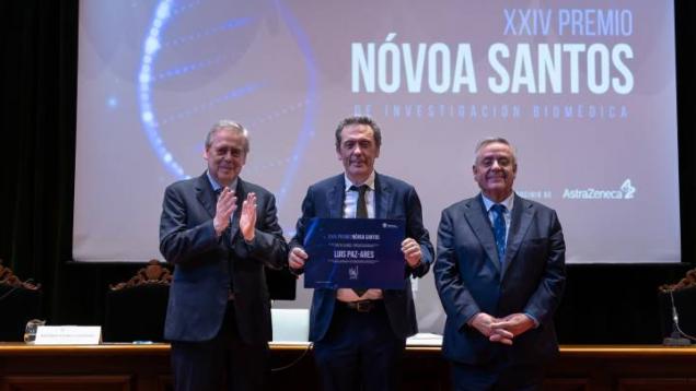 Tres hombres en escenario con pantalla detrás y el del medio con un diploma en las manos