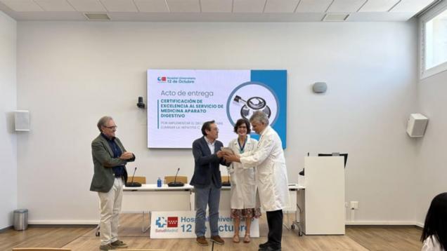 cuatro personas de pie en una sala con público en la entrega de un diploma